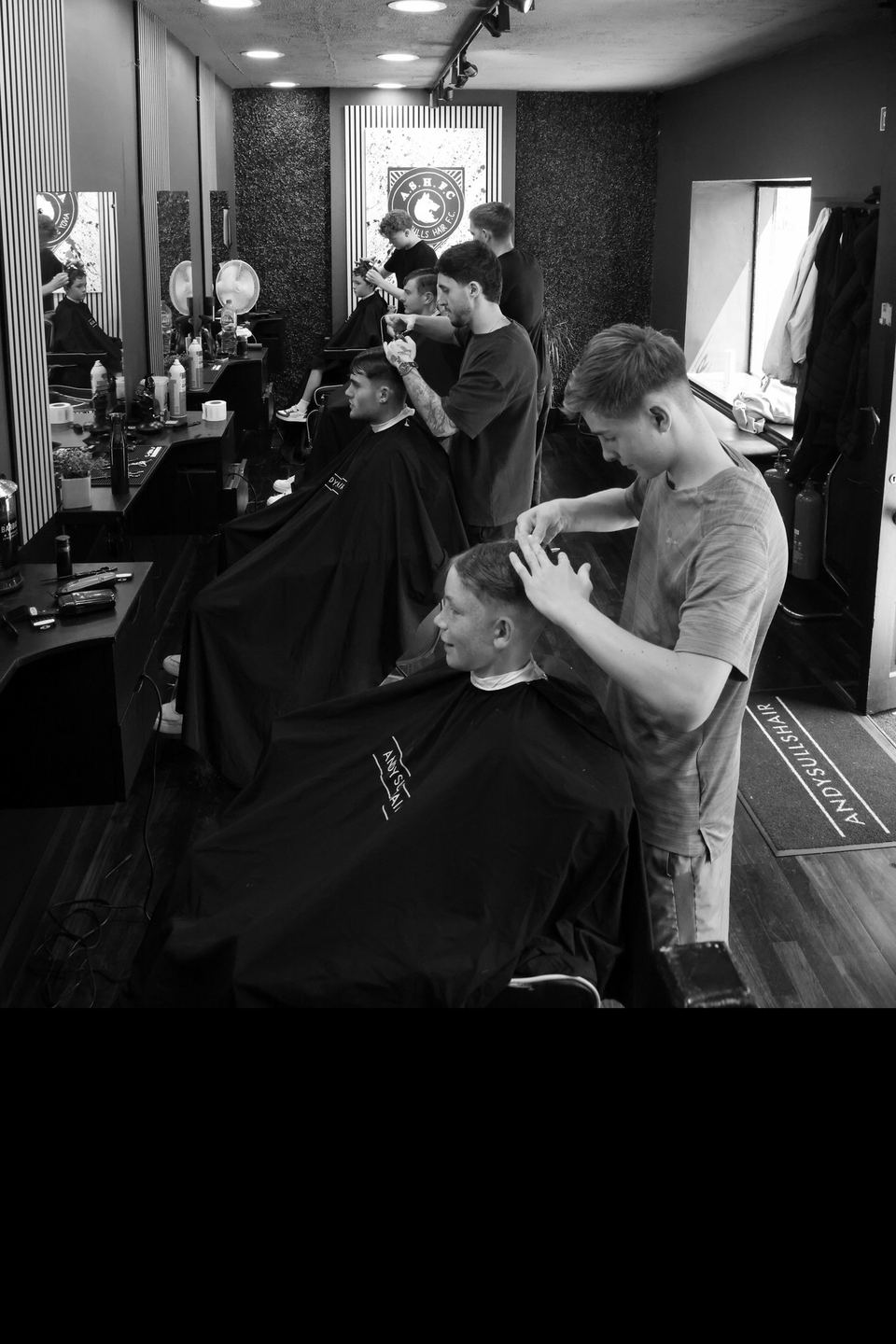 A row of academy students cutting clients' hair in the AndySullsHair shop on a class night