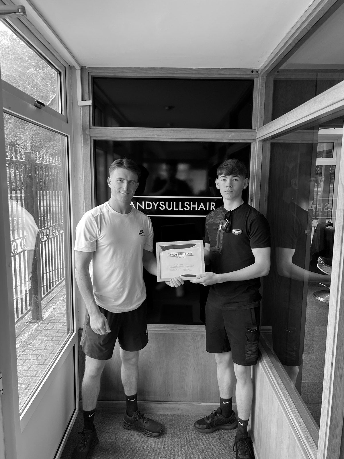 A graduate holding his certificate outside the AndySullsHair shop