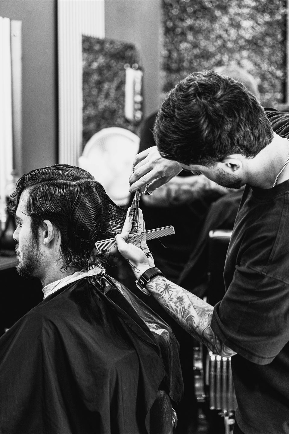 A barber at AndySullsHair scissor-cutting a client's hair, in black and white